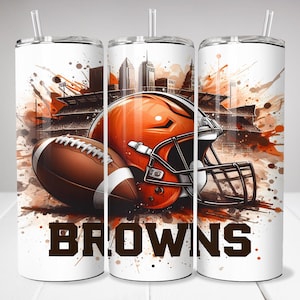 May include: A white tumbler with a brown football helmet and football, a cityscape, and the word "BROWNS" in brown letters. The background is a brown and orange watercolor design.