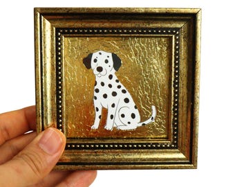 Peut inclure: Petite image encadrée carrée d'un chien dalmatien à taches noires sur fond doré. Le cadre doré est orné d'une bordure perlée. Le chien est assis, face à l'avant, la queue enroulée.