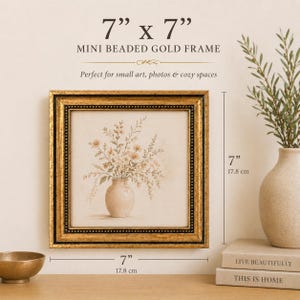 May include: A 7" x 7" mini beaded gold frame. The frame surrounds a print of a vase with flowers. The frame is gold with a black beaded border. The print is on a beige background.