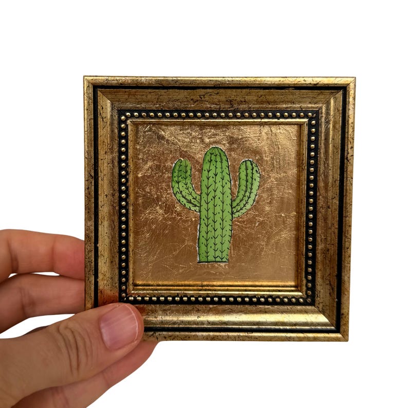 Peut inclure: Une &oelig;uvre d'art murale carr&eacute;e repr&eacute;sentant une illustration de cactus vert centr&eacute;e sur un fond en feuille d'or m&eacute;tallique. L'&oelig;uvre est encadr&eacute;e dans un cadre dor&eacute; orn&eacute; et vieilli avec une bordure int&eacute;rieure noire perl&eacute;e.
