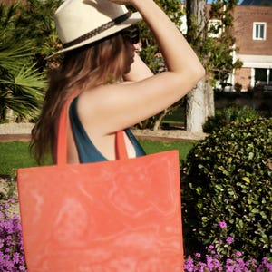 May include: A woman wearing a straw hat and sunglasses is carrying a large orange tote bag. The bag has a faded design on it.