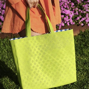 May include: A bright green tote bag with a white polka dot pattern. The bag has two handles and is made of a lightweight material.