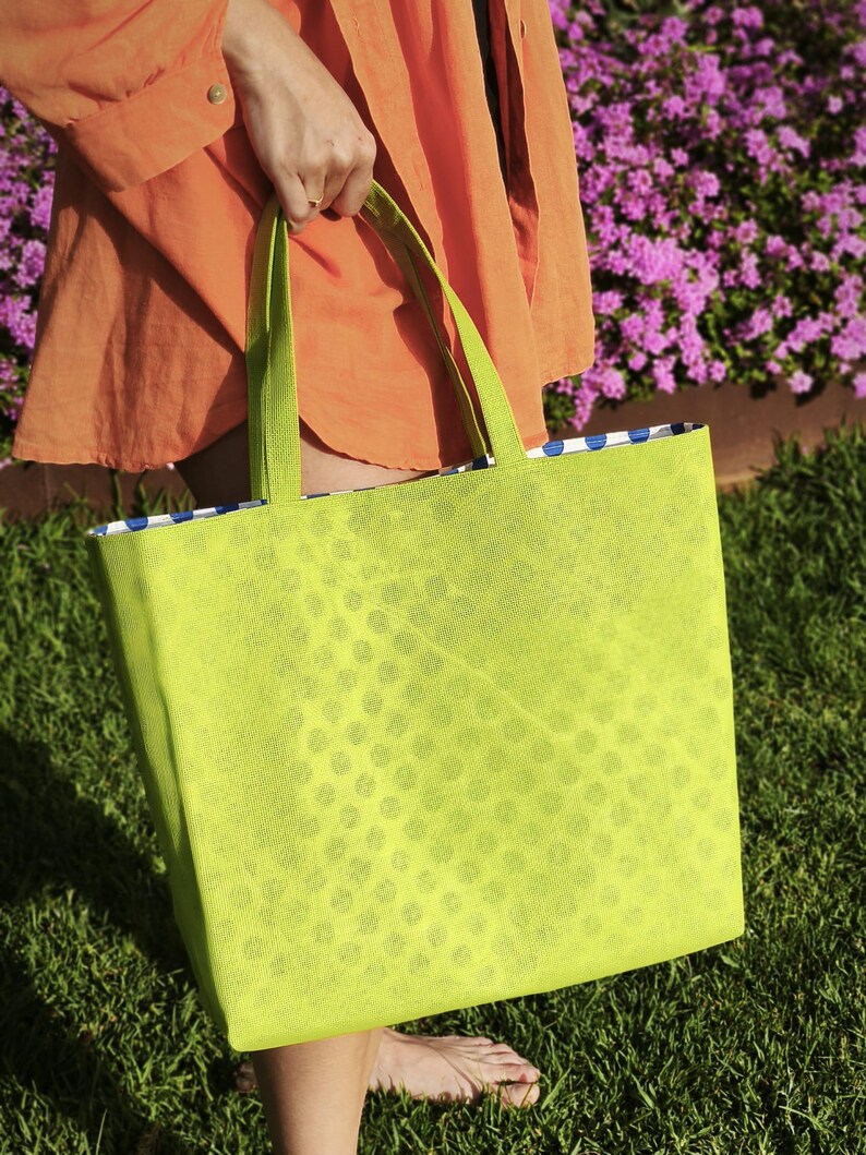 May include: A bright green tote bag with a white polka dot pattern. The bag has two handles and is made of a lightweight material.