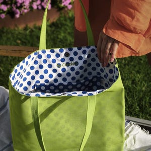 May include: A green canvas tote bag with blue polka dot lining. The bag has a white label with the text "by Conchita" on it.
