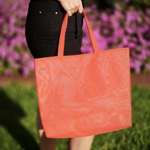 May include: A bright orange mesh tote bag with a wide handle. The bag is made of a lightweight, breathable material and is perfect for carrying groceries, books, or other items.
