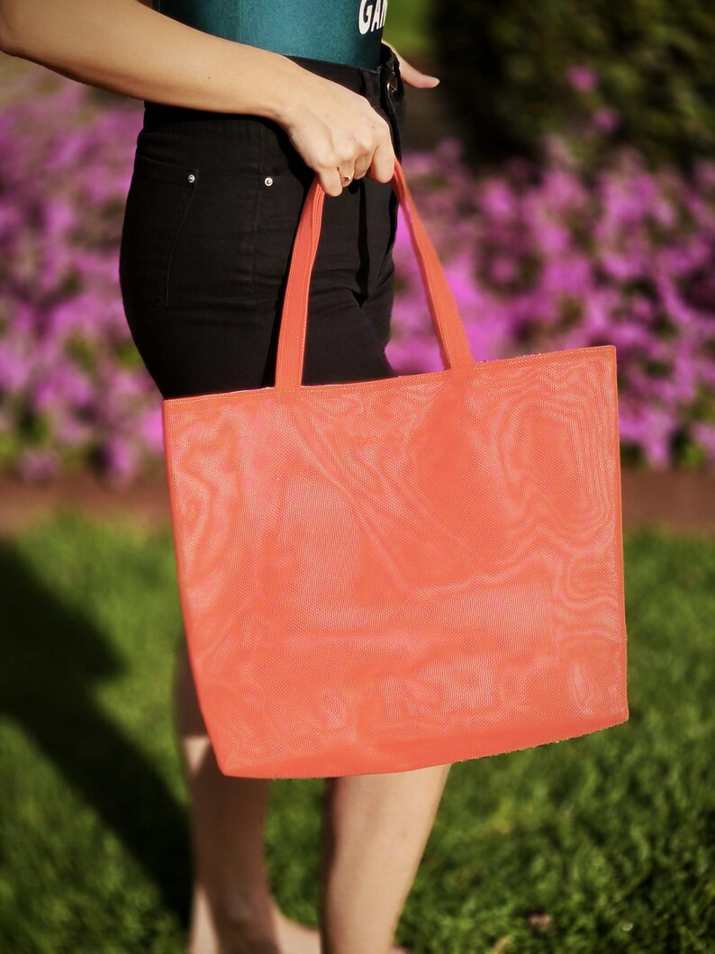 May include: A bright orange mesh tote bag with a wide handle. The bag is made of a lightweight, breathable material and is perfect for carrying groceries, books, or other items.