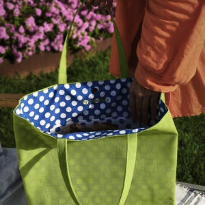 May include: A green tote bag with blue and white polka dot lining. The bag has two handles and is made of a textured fabric.