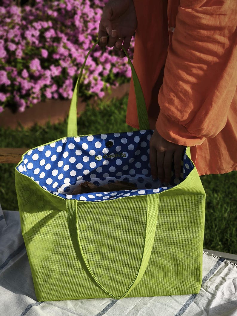 May include: A green tote bag with blue and white polka dot lining. The bag has two handles and is made of a textured fabric.