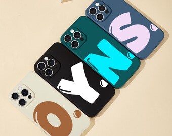 May include: Five different phone cases with colorful letters. The cases are all for the same model phone and have a variety of colors and designs. The letters on the cases spell out the word "SOY" in a playful, cartoon font.