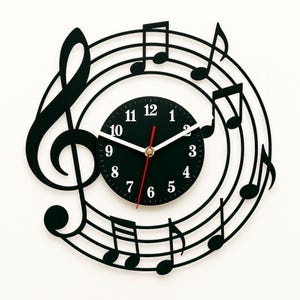 Può includere: Orologio da parete nero con un design a forma di nota musicale. Il quadrante dell'orologio è nero con numeri bianchi e una lancetta dei secondi rossa.
