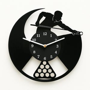 Könnte beinhalten: Schwarze Schallplattenuhr mit einer Silhouette einer Person, die Billard spielt. Das Zifferblatt der Uhr hat weiße Zahlen und Zeiger. Die Uhr ist mit einem Dreieck aus weißen Billardkugeln verziert.