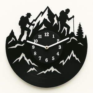 Op de afbeelding: Zwarte vinyl platen klok met een silhouet van twee wandelaars die een berg beklimmen. De wijzerplaat van de klok heeft witte cijfers en wijzers.