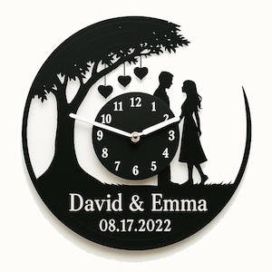 May include: Black vinyl record clock with a silhouette of a tree, two people, and hearts. The clock face reads "David & Emma 08.17.2022".