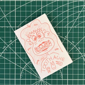 May include: A red and white illustration of a cartoon character with a toothache. The character has a large mouth with many teeth and is holding a tooth in their hand. The text "TOOTH ACHE" is written in a stylized font.