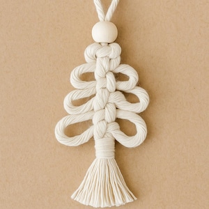 Könnte beinhalten: Handgefertigter Weihnachtsbaumschmuck aus Makramee in Off-White. Das Baumdesign hat Schlaufenknoten und eine Quaste am unteren Ende. Oben befindet sich eine Holzperle. Das Wort "Weiß" wird in einem weißen Rechteck unten angezeigt.
