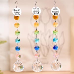 May include: Three memorial suncatchers with rainbow-colored crystal beads and a clear crystal ball with a paw print. Each suncatcher has a circular charm with a pet's name and dates or a message like "Look for me in the rainbows."