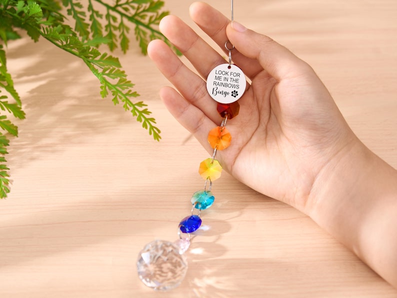 May include: A rainbow crystal suncatcher with a clear crystal ball at the bottom. The suncatcher has a series of colorful faceted beads and a circular charm with the text "LOOK FOR ME IN THE RAINBOWS Bingo".
