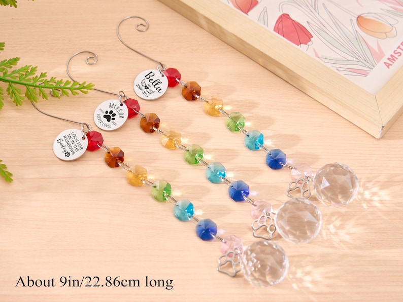 May include: Three decorative pet memorial suncatchers, each about 9 inches long, with a rainbow of faceted beads and a clear crystal ball. Each has a metal charm with a pet's name and paw print.