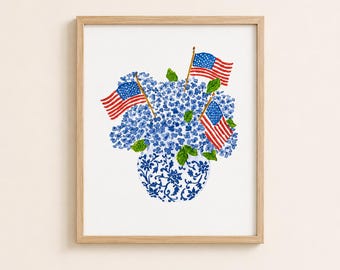 May include: A framed watercolour print depicting a blue and white floral vase filled with blue hydrangeas and three small American flags. The artwork has a patriotic theme, with red, white, and blue colours.