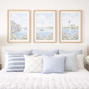 May include: Three framed watercolor prints of coastal scenes with sailboats and buildings hang above a bed with blue and white pillows. Two woven lamps sit on white nightstands. The room has a coastal theme.