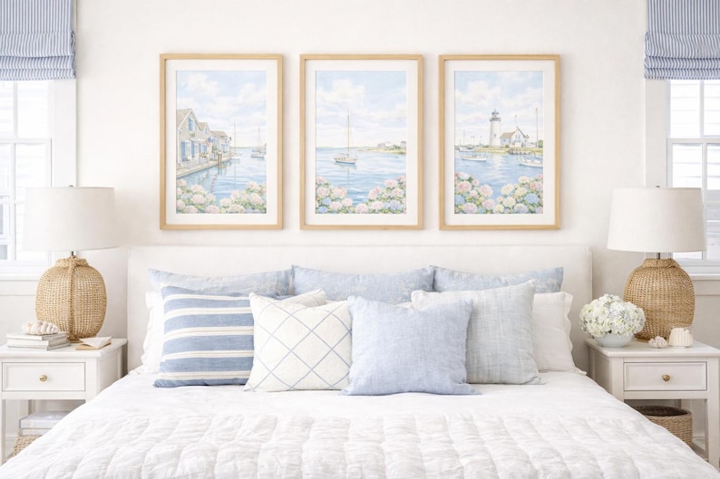 May include: Three framed watercolor prints of coastal scenes with sailboats and buildings hang above a bed with blue and white pillows. Two woven lamps sit on white nightstands. The room has a coastal theme.
