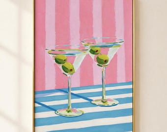 May include: A framed art print depicting two martini glasses with green olives. The glasses are set against a pink and white striped background, with a blue and white striped surface below. The artwork is in a gold frame.