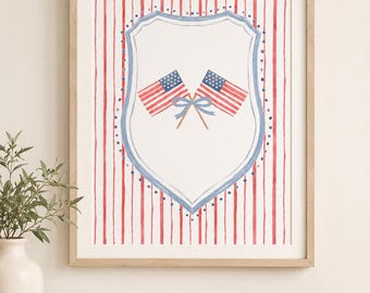 May include: Framed artwork with a patriotic theme. The print displays two crossed American flags inside a shield, set against red and white vertical stripes. The frame is a light wood colour.