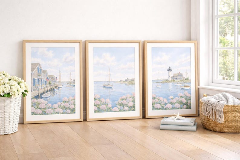 May include: Three framed watercolor prints depicting coastal scenes. The artwork features a harbor with boats, a sailboat on the water, and a lighthouse. The prints are in light wood frames, resting on a wooden floor.