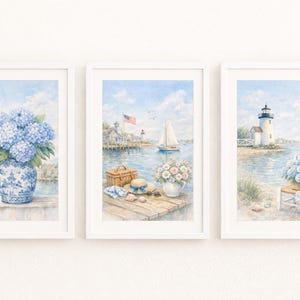 Puede incluir: Conjunto de tres impresiones en acuarela enmarcadas. Las impresiones representan escenas costeras con una paleta de colores azul y blanco. Una presenta hortensias azules en un jarrón, otra una escena portuaria con un velero y la tercera un faro.