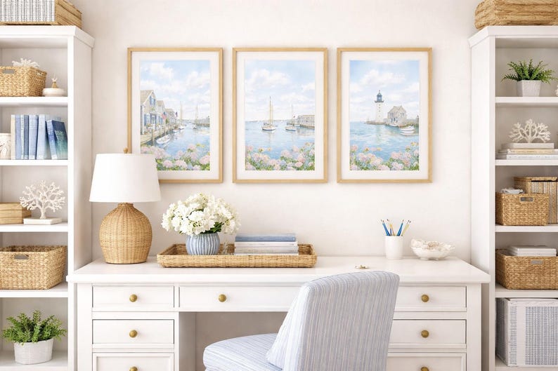 May include: Three framed watercolor prints depicting coastal scenes with boats, buildings, and a lighthouse. The prints are displayed above a white desk with a woven lamp, flowers, and a striped chair. The room has white shelves and woven baskets.