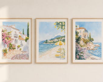 May include: Three framed watercolour prints of coastal scenes. One shows a white building with pink flowers, another a beach with a yellow parasol, and the last a villa by the sea. All are in light wood frames.