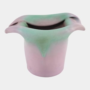 May include: A handmade ceramic vase in a tulip shape. The vase is primarily light pink with a green and lavender rim. The rim has a unique, wavy design. The vase is a decorative item.