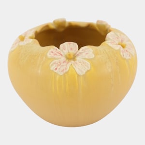 May include: A round, yellow ceramic bowl featuring a textured surface with vertical ridges. The rim is decorated with several raised, light pink flower appliques, each with a small yellow center, evenly spaced around the top edge of the vessel.