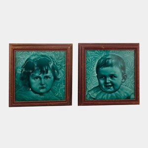 May include: Two framed portraits of children. Each portrait features a teal-colored image of a child against a teal floral patterned background. The frames are made of dark brown wood. The children's portraits are in a square format.