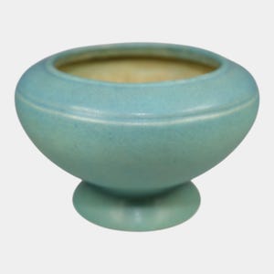 May include: A light blue ceramic bowl with a round base and a wide, open top. The bowl has a smooth, matte finish and a subtle crackle effect. The interior is a light beige color. A decorative piece for the home.