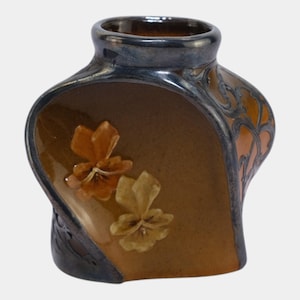 May include: A ceramic vase with a unique shape and a glossy finish. The vase features a brown body with two raised flower designs in shades of orange and yellow. The rim and edges are a dark blue-gray color, with an orange decorative pattern.