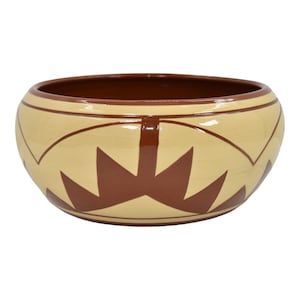 May include: A ceramic bowl with a cream-colored exterior and a brown interior. The exterior features a repeating geometric pattern in brown. The bowl has a rounded shape and a wide opening, suitable for serving or display.