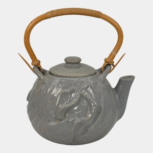 May include: A gray ceramic teapot with a lid and a curved, woven handle. The teapot has a rounded body with a textured floral design. The handle is made of light brown woven material.
