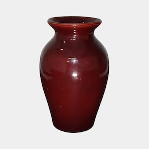 May include: A glossy, maroon-colored ceramic vase. The vase has a rounded body that tapers towards a narrow neck and flared rim. The surface reflects light, highlighting its smooth texture and rich color.