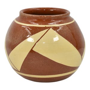 May include: A round, brown ceramic vase with a geometric design. The vase features a light brown and dark brown color scheme with a cream-colored geometric pattern. The vase has a wide opening and a smooth, glossy finish.