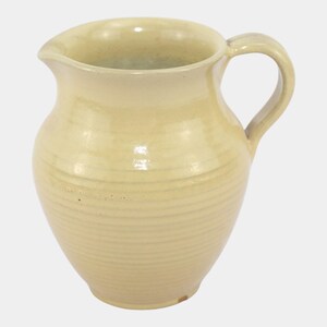 May include: A cream-colored ceramic pitcher with a handle and a spout. The pitcher has horizontal ridges around its body and a smooth, glossy finish. The design is simple and classic, suitable for serving beverages.