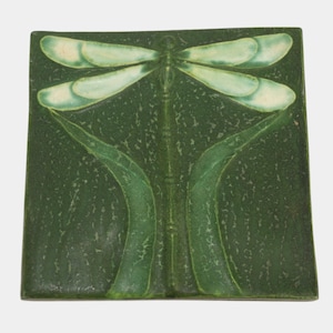 May include: Square ceramic tile with a dragonfly design. The dragonfly has light green wings and a dark green body, set against a textured dark green background. The tile also features stylized green leaves.