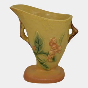 May include: A yellow ceramic vase with a floral design and two handles. The vase has a wide mouth and a narrow base.