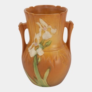 May include: A ceramic vase with a matte orange and brown finish, featuring two side handles and a scalloped rim. The body is decorated with a raised, molded relief of white iris flowers and green leaves that extend from the base to the neck.