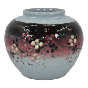 May include: A small, light blue ceramic vase with a black, pink, and white floral design. The vase has a round body and a slightly flared lip.