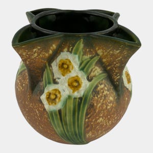 May include: A ceramic vase with a brown speckled exterior and a dark green interior. The vase features a floral design of white daffodils with yellow centers and green leaves. The vase has a unique shape with multiple openings.