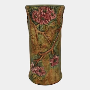 May include: A tall, cylindrical vase with a textured, bark-like appearance. The vase is painted in shades of green and brown, with raised floral and branch details in pink and red. The vase is a decorative item.