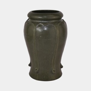 May include: A dark green vase with a wide, rounded rim and a bulbous body. The vase features vertical, curved decorative elements and small, rounded feet. The surface has a textured appearance.