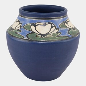 May include: A navy blue ceramic vase with a wide base and a narrow opening. The upper portion features a decorative band with white water lilies, green lily pads, and a blue background. The vase is approximately 6 inches tall.