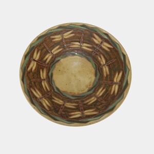 May include: A round ceramic bowl with a dragonfly design. The bowl features a light brown center, a dark brown band with dragonfly illustrations, and a green and brown outer rim. The dragonfly illustrations are in a cream color.